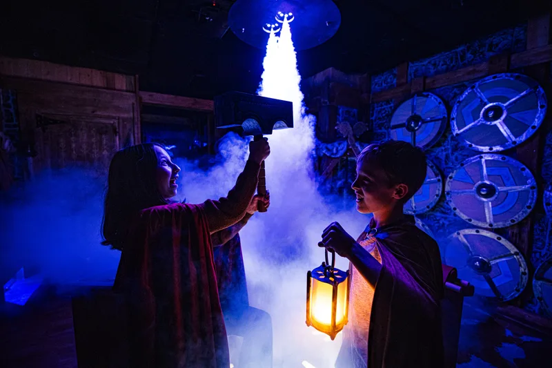 Two players lift a glowing hammer through the mist in Ragnarok