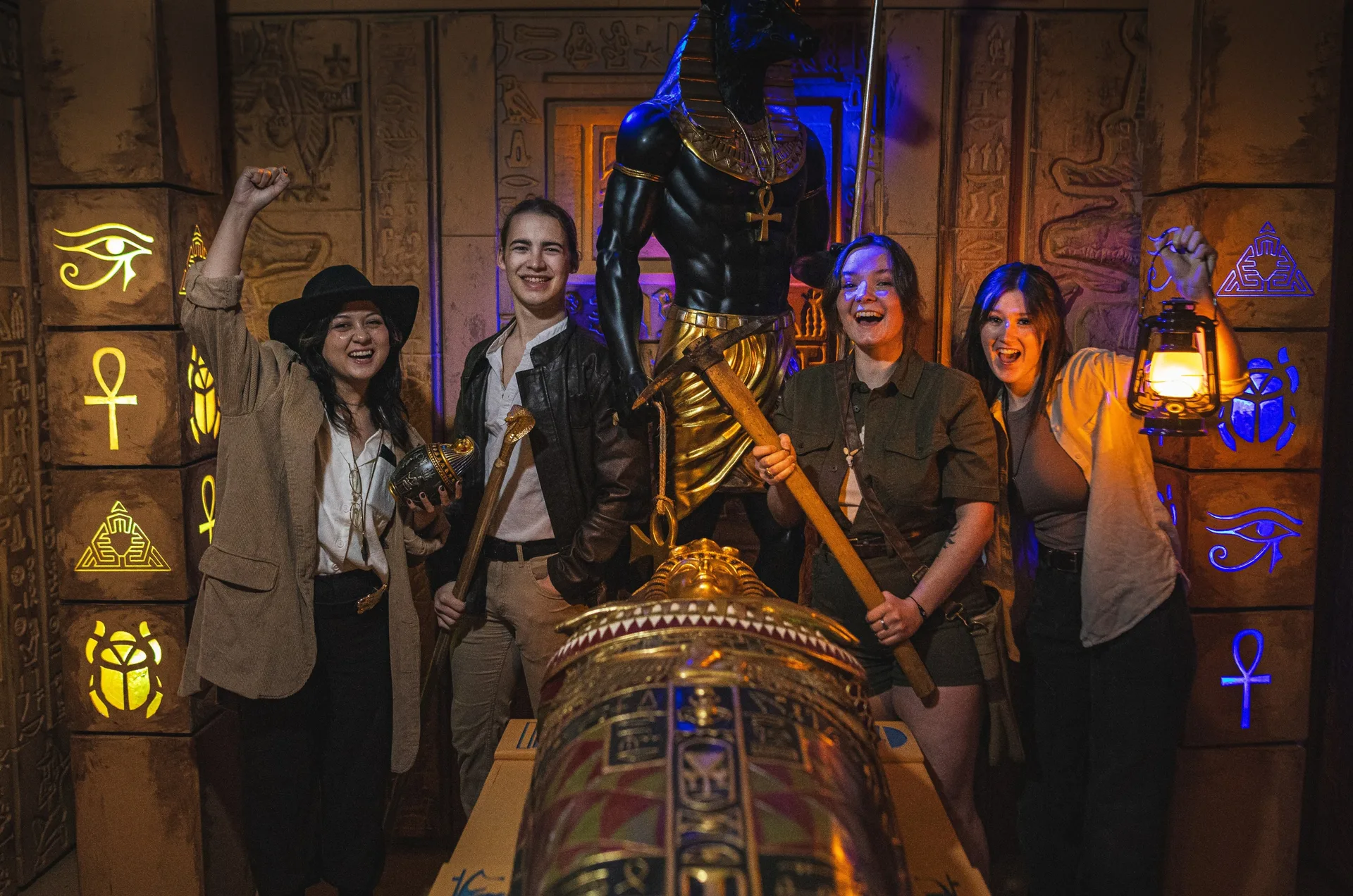Four friends in explorer gear celebrating around the gold sarcophagus