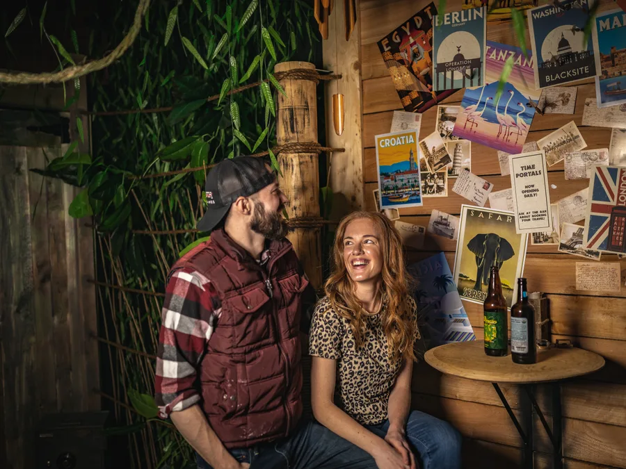 A couple laughing together on a bench by the travel poster wall